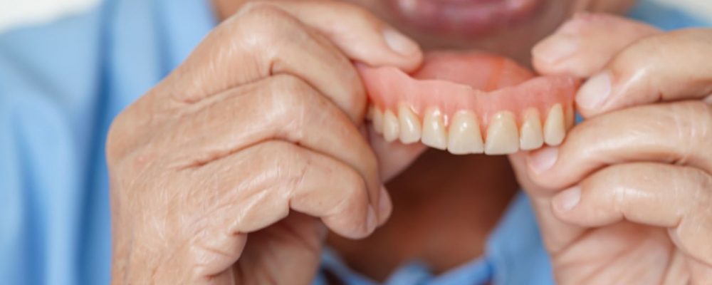 Person in light blue scrubs removes denture from own mouth