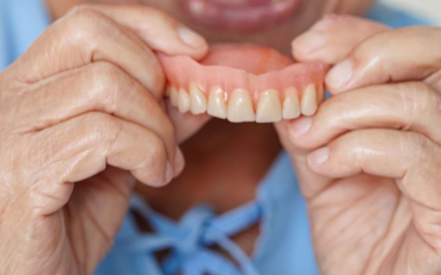 Person in light blue scrubs removes denture from own mouth