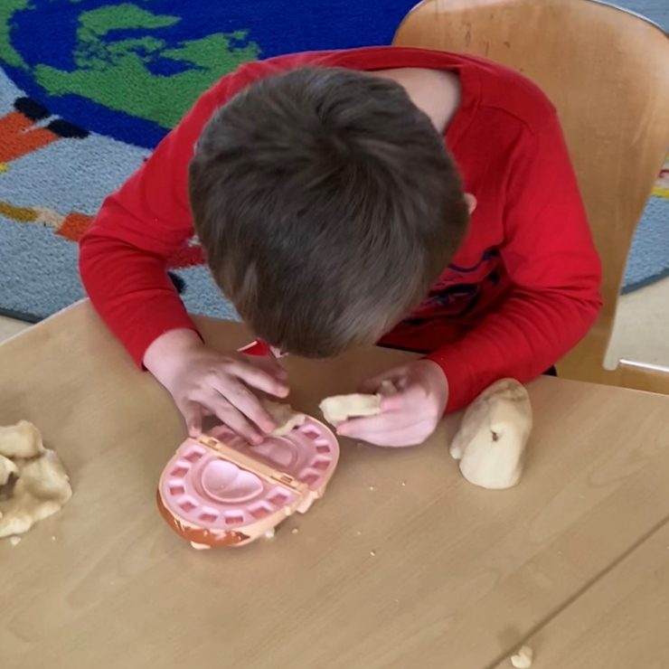 A child leans over a playdough set which depicts mouths for which he can make and take care of teeth