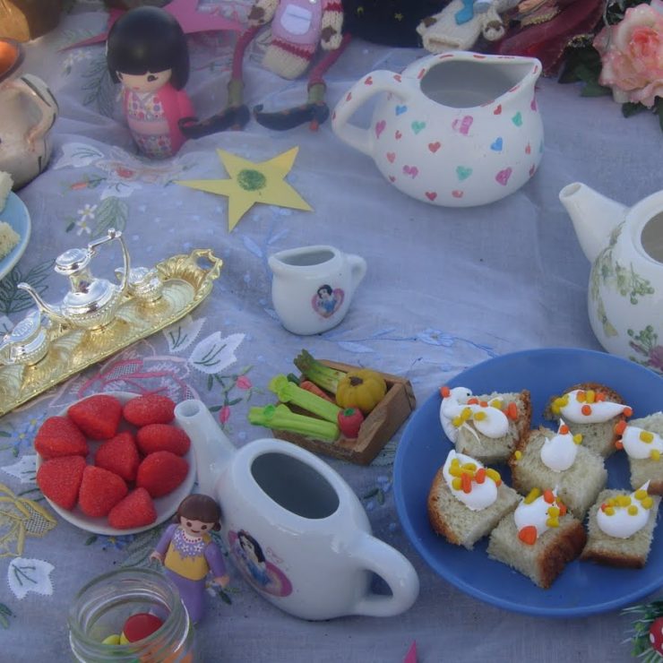 A sheet is laid out with a picnic, tea pots, glittery stars and fairy themed items.